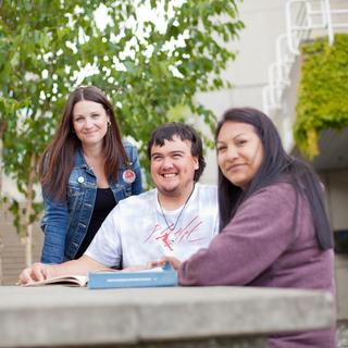 Three students chat around a table outside