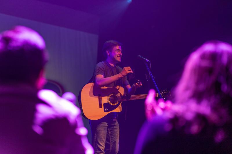 Man with guitar on stage with backs of members of crowd visible