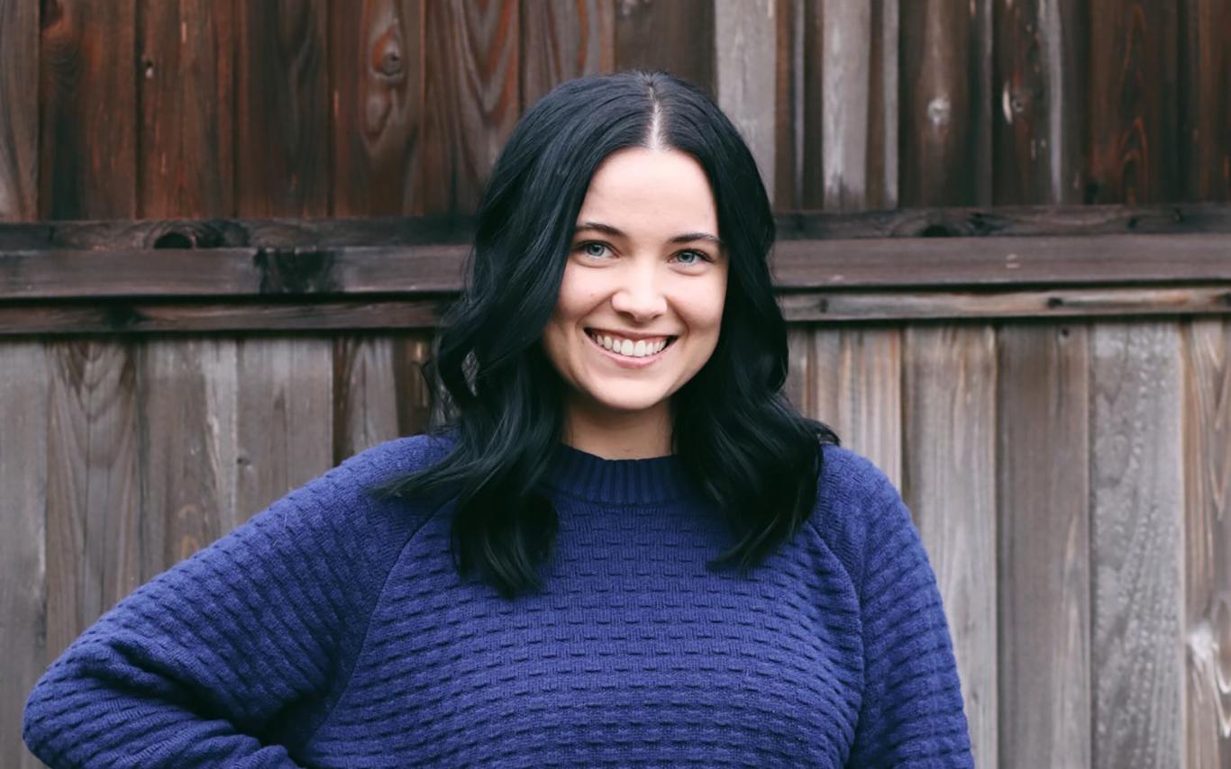 Alisha wearing a blue sweater standing in front of a fence