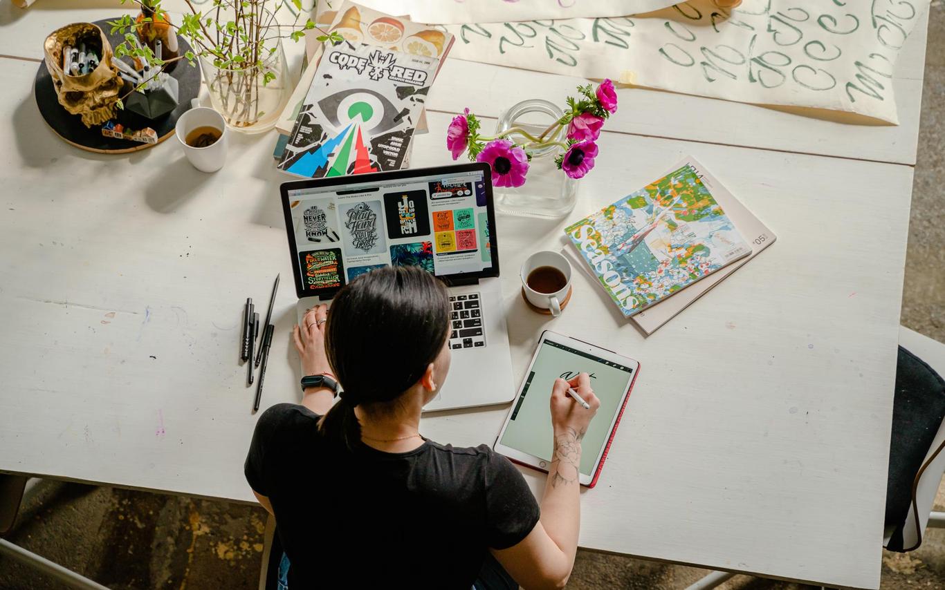 above view of a person with a laptop in front of them, notepad next to them and crafting materials around them
